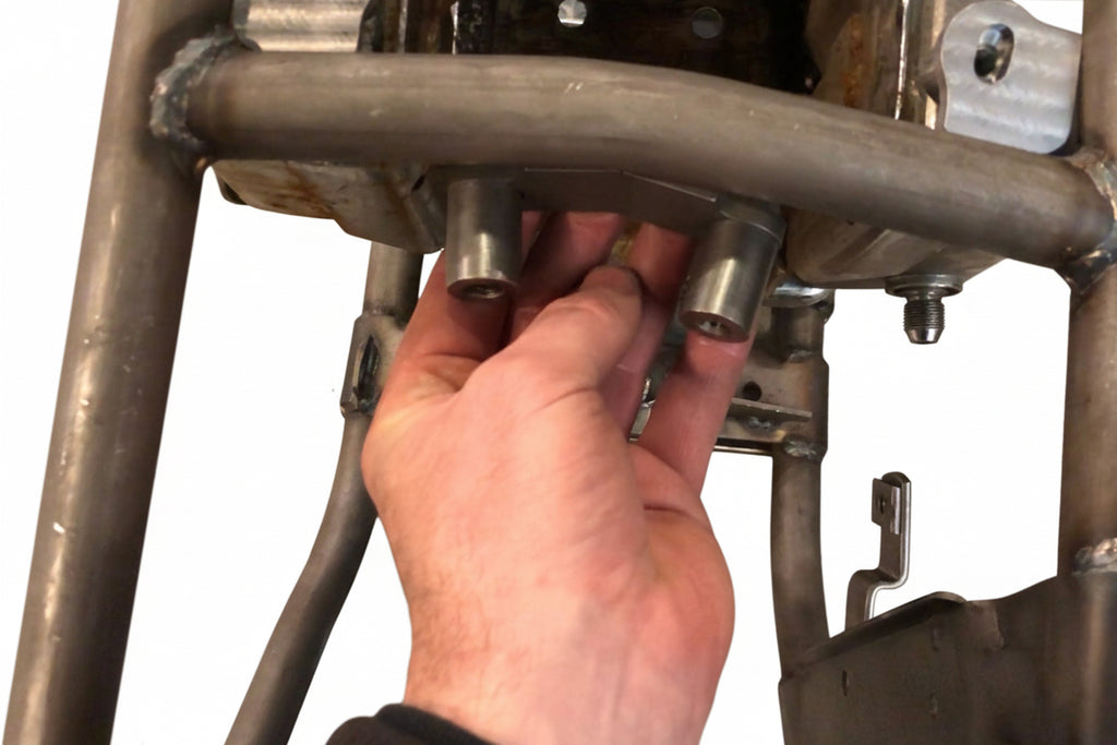 A person's hand installing a metal mounting kit on a motorcycle frame.